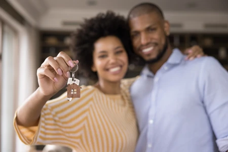 Black couple holding up a set of keys with a house keychain attached